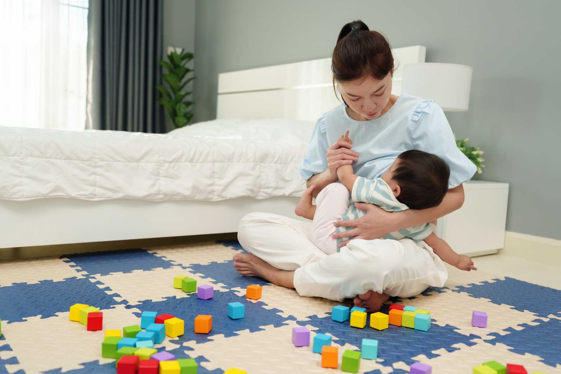 mother breastfeeding infant baby after playing wooden block in bedroom