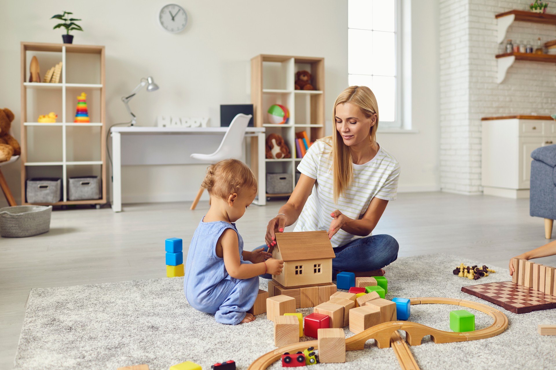 Young mom playing with cute little son and teaching him to build toy house in cozy modern apartment