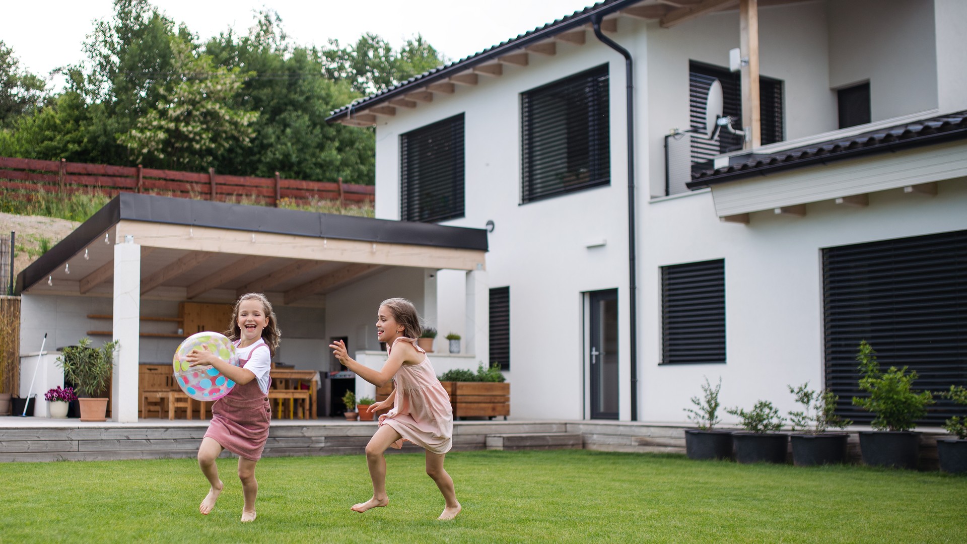 Two small girls sisters playing with a ball outdoors in the backyard, running.